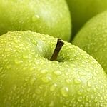 Vibrant close-up image of fresh green apples covered in water droplets, showcasing their freshness and texture.